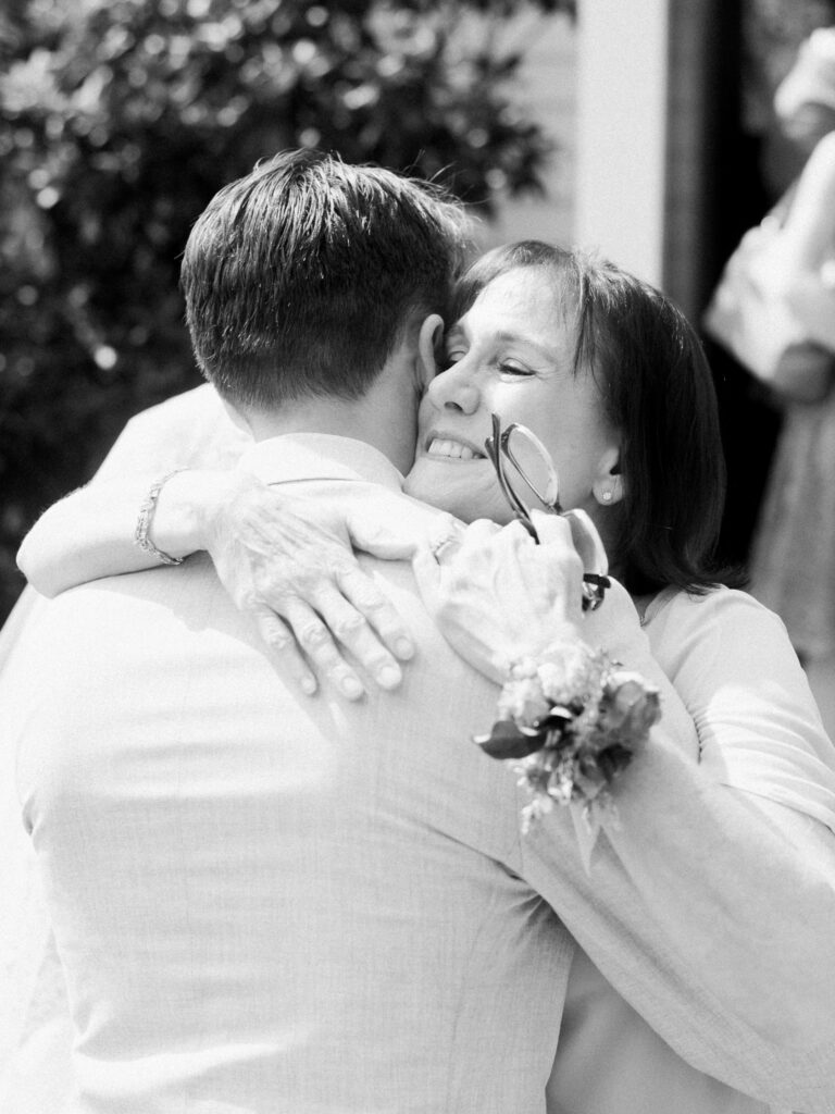 Candid moment of groom hugging mom in front of Saint Anthony's Catholic Church in Mendocino, California, by destination wedding photographer, Bethany Erin Photography.